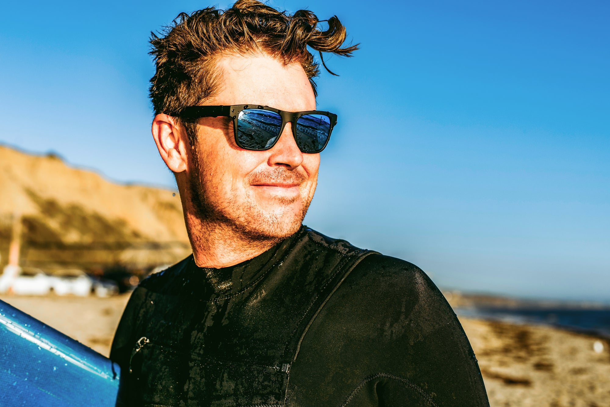 Male surfer wearing sunglasses staring out into the horizon.